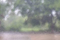 A estação das chuvas, água natural das gotas da chuva do respingo deixa cair na janela de vidro no fundo da árvore da estação das fotografia de stock royalty free A estação das chuvas, água natural das gotas da chuva do respingo deixa cair na janela de vidro no fundo da árvore da estação das fotografia de stock royalty free