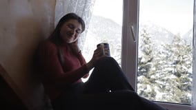 Estilo de vida acolhedor do inverno Xícara de café bebendo da mulher feliz nova que veste a camiseta feita malha que senta-se em video estoque Estilo de vida acolhedor do inverno Xícara de café bebendo da mulher feliz nova que veste a camiseta feita malha que senta-se em video estoque