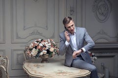 Estimado hombre joven con un corte de pelo en un traje, sentándose en una tabla en un cuarto con un interior clásico lujo Belleza imagenes de archivo Estimado hombre joven con un corte de pelo en un traje, sentándose en una tabla en un cuarto con un interior clásico lujo Belleza imagenes de archivo
