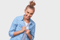Estudiante apuesto con el peinado del bollo que sonríe positivamente y que está en gran humor mientras que se coloca sobre el fon foto de archivo Estudiante apuesto con el peinado del bollo que sonríe positivamente y que está en gran humor mientras que se coloca sobre el fon foto de archivo