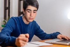 Estudiante que hace la preparación en su escritorio con el ordenador portátil fotografía de archivo Estudiante que hace la preparación en su escritorio con el ordenador portátil fotografía de archivo