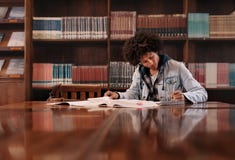 Estudiante universitario que hace la asignación en biblioteca foto de archivo libre de regalías Estudiante universitario que hace la asignación en biblioteca foto de archivo libre de regalías