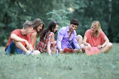 Estudiantes de los amigos que se preparan para el examen que se sienta en el césped en el parque fotos de archivo Estudiantes de los amigos que se preparan para el examen que se sienta en el césped en el parque fotos de archivo
