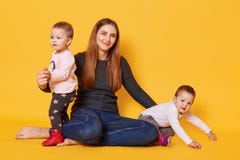 Estudio tirado de madre joven y de sus actitudes gemelas de los niños en el estudio de la foto isoleted sobre fondo amarillo La m fotografía de archivo Estudio tirado de madre joven y de sus actitudes gemelas de los niños en el estudio de la foto isoleted sobre fondo amarillo La m fotografía de archivo