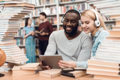 Ethnic african american guy and white girl surrounded by books in library. Students are using tablet. royalty free stock photo Ethnic african american guy and white girl surrounded by books in library. Students are using tablet. royalty free stock photo
