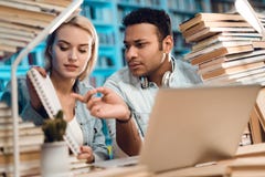 Etnisk indisk grabb för blandat lopp och vitflicka som omges av böcker i arkiv Studenter ser anmärkningar royaltyfria bilder Etnisk indisk grabb för blandat lopp och vitflicka som omges av böcker i arkiv Studenter ser anmärkningar royaltyfria bilder