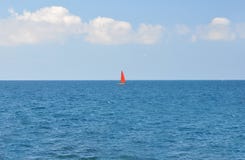 Ett fartyg med ett rött seglar att sväva längs det blåa havet på en bakgrund för blå himmel royaltyfria bilder Ett fartyg med ett rött seglar att sväva längs det blåa havet på en bakgrund för blå himmel royaltyfria bilder