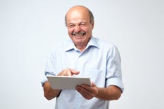 Euphoric winner mature caucasian man laughing with a tablet. He saw very funny video or joke. Stock Photo Euphoric winner mature caucasian man laughing with a tablet. He saw very funny video or joke. Stock Photo