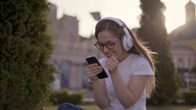 Excited beautiful girl receiving a sms message with good news in a mobile phone outside in a park with a green stock footage Excited beautiful girl receiving a sms message with good news in a mobile phone outside in a park with a green stock footage