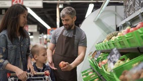 Experienced shop assistant is selling fruit to cheerful young family mom and child, giving them pears, apples and stock footage Experienced shop assistant is selling fruit to cheerful young family mom and child, giving them pears, apples and stock footage
