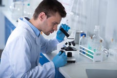 Explorador serio joven que se sienta por el microscopio y que trabaja con él fotografía de archivo Explorador serio joven que se sienta por el microscopio y que trabaja con él fotografía de archivo