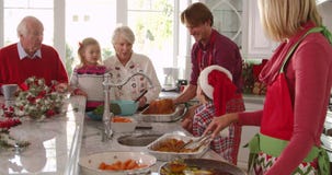 Extended family group prepare Christmas lunch in kitchen - Father takes turkey from oven and bastes it with spoon