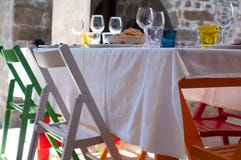 Exterior of a restaurant with a laid out table ready for lunch, with colorful chairs of red, white and natural wood color royalty free stock photos Exterior of a restaurant with a laid out table ready for lunch, with colorful chairs of red, white and natural wood color royalty free stock photos