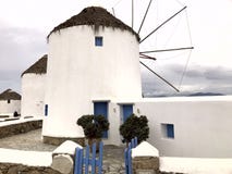 Fachada branca colorida de um moinho antigo branco com as portas azuis contra o céu na ilha de Mykonos foto de stock Fachada branca colorida de um moinho antigo branco com as portas azuis contra o céu na ilha de Mykonos foto de stock
