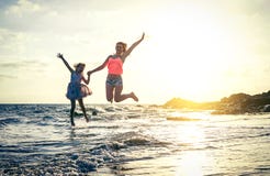 Famiglia amorosa felice della madre e della figlia che saltano nell'acqua al tramonto sulla spiaggia - mamma con il suo bambino d fotografia stock Famiglia amorosa felice della madre e della figlia che saltano nell'acqua al tramonto sulla spiaggia - mamma con il suo bambino d fotografia stock