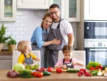 Famiglia felice con i bambini che preparano insalata di verdure fotografia stock Famiglia felice con i bambini che preparano insalata di verdure fotografia stock
