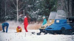 Familia del bosque del invierno en la ropa colorida que juega bolas de nieve en la cámara lenta Motos de nieve en el primero plan metrajes Familia del bosque del invierno en la ropa colorida que juega bolas de nieve en la cámara lenta Motos de nieve en el primero plan metrajes