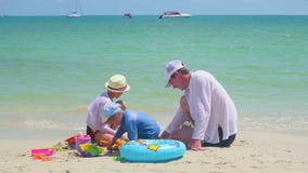 Familia feliz con los niños que juegan en la playa arenosa con los juguetes Isla tropical, en un día caliente almacen de video Familia feliz con los niños que juegan en la playa arenosa con los juguetes Isla tropical, en un día caliente almacen de video
