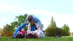 Familia feliz que miente en el césped La madre y el padre que detienen a su hijo en sus brazos sobre su cabeza, el niño sonríe En metrajes Familia feliz que miente en el césped La madre y el padre que detienen a su hijo en sus brazos sobre su cabeza, el niño sonríe En metrajes