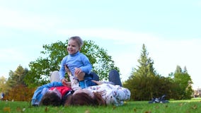 Familia feliz que miente en el césped La madre y el padre que detienen a su hijo en sus brazos sobre su cabeza, el niño sonríe En metrajes Familia feliz que miente en el césped La madre y el padre que detienen a su hijo en sus brazos sobre su cabeza, el niño sonríe En metrajes