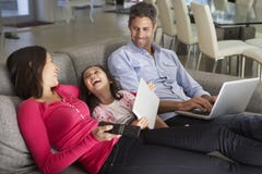 Familie auf Sofa With Laptop And Digital-Tablet fernsehend Lizenzfreies Stockbild Familie auf Sofa With Laptop And Digital-Tablet fernsehend Lizenzfreies Stockbild