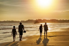 Familievakantie in de keerkringen door het overzees - silhouetten van mensen die op het strand bij zonsondergang lopen stock fotografie Familievakantie in de keerkringen door het overzees - silhouetten van mensen die op het strand bij zonsondergang lopen stock fotografie