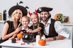 familj i olika halloween dräkter på tabellen med den svarta krukan med fester i kök royaltyfria foton familj i olika halloween dräkter på tabellen med den svarta krukan med fester i kök royaltyfria foton
