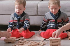 Familjmamman, farsan och två tvilling- bröder spelar byggande tillsammans ut ur träkvarter på golvet Händer för närbildförälder` royaltyfri foto Familjmamman, farsan och två tvilling- bröder spelar byggande tillsammans ut ur träkvarter på golvet Händer för närbildförälder` royaltyfri foto