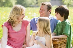 Famille s'asseyant à l'extérieur avec le sourire de panier de pique-nique Famille s'asseyant à l'extérieur avec le sourire de panier de pique-nique