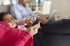 Famille sur Sofa With Smartphone, l'ordinateur portable et la Tablette de Digital photo stock Famille sur Sofa With Smartphone, l'ordinateur portable et la Tablette de Digital photo stock