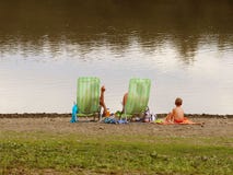 Family: father, mother and son are resting on beach chairs on the shore by the pond. Family holiday on the water. Beach of sand an stock photo Family: father, mother and son are resting on beach chairs on the shore by the pond. Family holiday on the water. Beach of sand an stock photo