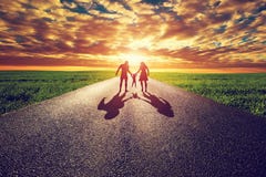 Family walk on long straight road, way towards sunset sun