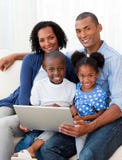 Família afro-americana que usa um portátil no sofá imagem de stock Família afro-americana que usa um portátil no sofá imagem de stock