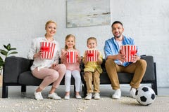 família feliz com as caixas da pipoca que sentam-se no sofá e no sorriso imagens de stock família feliz com as caixas da pipoca que sentam-se no sofá e no sorriso imagens de stock