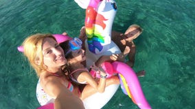 Família feliz com a menina que toma o selfie no assento do mar no unicórnio inflável filme Família feliz com a menina que toma o selfie no assento do mar no unicórnio inflável filme