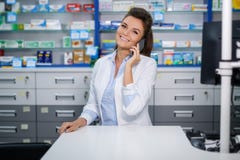 Farmacéutico sonriente hermoso de la mujer joven que habla en el teléfono celular en farmacia fotos de archivo Farmacéutico sonriente hermoso de la mujer joven que habla en el teléfono celular en farmacia fotos de archivo