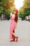 Fashion city portrait of stylish hipster woman with milk shake, red striped dress, red cap and sneakers, makeup, long stock photos Fashion city portrait of stylish hipster woman with milk shake, red striped dress, red cap and sneakers, makeup, long stock photos