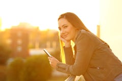 Fashion girl holding a phone looking at camera at sunset stock image Fashion girl holding a phone looking at camera at sunset stock image