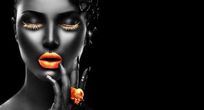 Fashion model with black skin, golden lips, eyelashes and jewellery - golden ring on hand. on black background
