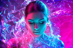 Fashion model woman in colorful bright neon lights posing in studio through transparent film. Portrait of beautiful sexy girl