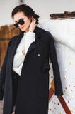 Fashion pretty woman model wearing a dark coat and white sweater, in sunglasses, posing over white background royalty free stock images Fashion pretty woman model wearing a dark coat and white sweater, in sunglasses, posing over white background royalty free stock images