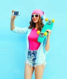 Fashion pretty cool girl with skateboard makes self portrait on smartphone over blue Stock Photos Fashion pretty cool girl with skateboard makes self portrait on smartphone over blue Stock Photos