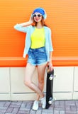 Fashion pretty woman with a skateboard in the city over orange colorful royalty free stock image Fashion pretty woman with a skateboard in the city over orange colorful royalty free stock image