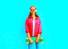 Fashion smiling woman with a skateboard listens to music in wireless headphones in pink denim jacket Royalty Free Stock Image Fashion smiling woman with a skateboard listens to music in wireless headphones in pink denim jacket Royalty Free Stock Image