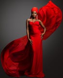 Fashion Woman in Red Dress and Hijab. African Model in Evening long Gown with flowing Silk Fabric over Dark Gray background. Muslim Bride in Wedding chiffon