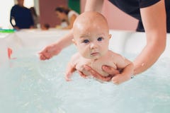 A father helps is infant boy during swimming lessons in the pool.