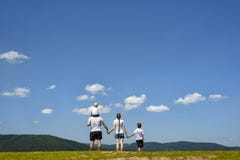 Father, mother and two little sons are standing on a green field on a background of wooded hills, blue sky and clouds. Family royalty free stock images Father, mother and two little sons are standing on a green field on a background of wooded hills, blue sky and clouds. Family royalty free stock images