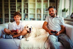 Father and son sitting on sofa with pet dog and playing video games royalty free stock image Father and son sitting on sofa with pet dog and playing video games royalty free stock image