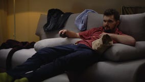 Fauler unordentlicher Junggeselle, der auf, Couch nach der Arbeit zu liegen fernsieht und Chips zu essen stock video Fauler unordentlicher Junggeselle, der auf, Couch nach der Arbeit zu liegen fernsieht und Chips zu essen stock video