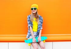 Façonnez la fille assez blonde avec la planche à roulettes dans la ville au-dessus de l'orange colorée Photo libre de droits Façonnez la fille assez blonde avec la planche à roulettes dans la ville au-dessus de l'orange colorée Photo libre de droits
